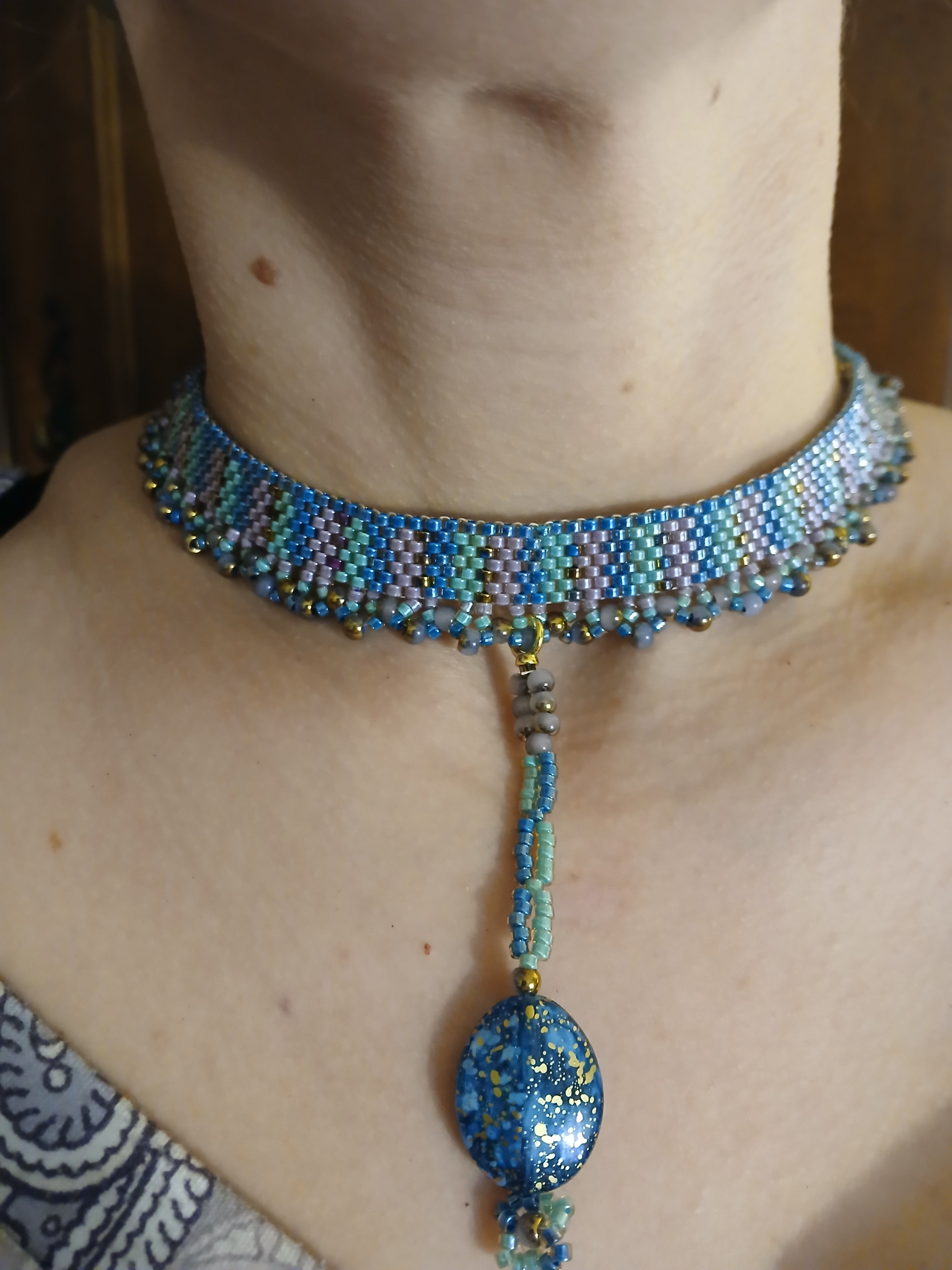 Handwoven choker in seafoam teal and purple from the Mermaid Finery Collection by Regina Creates, featuring a 3.5-inch bead pendant. Closeup on model 