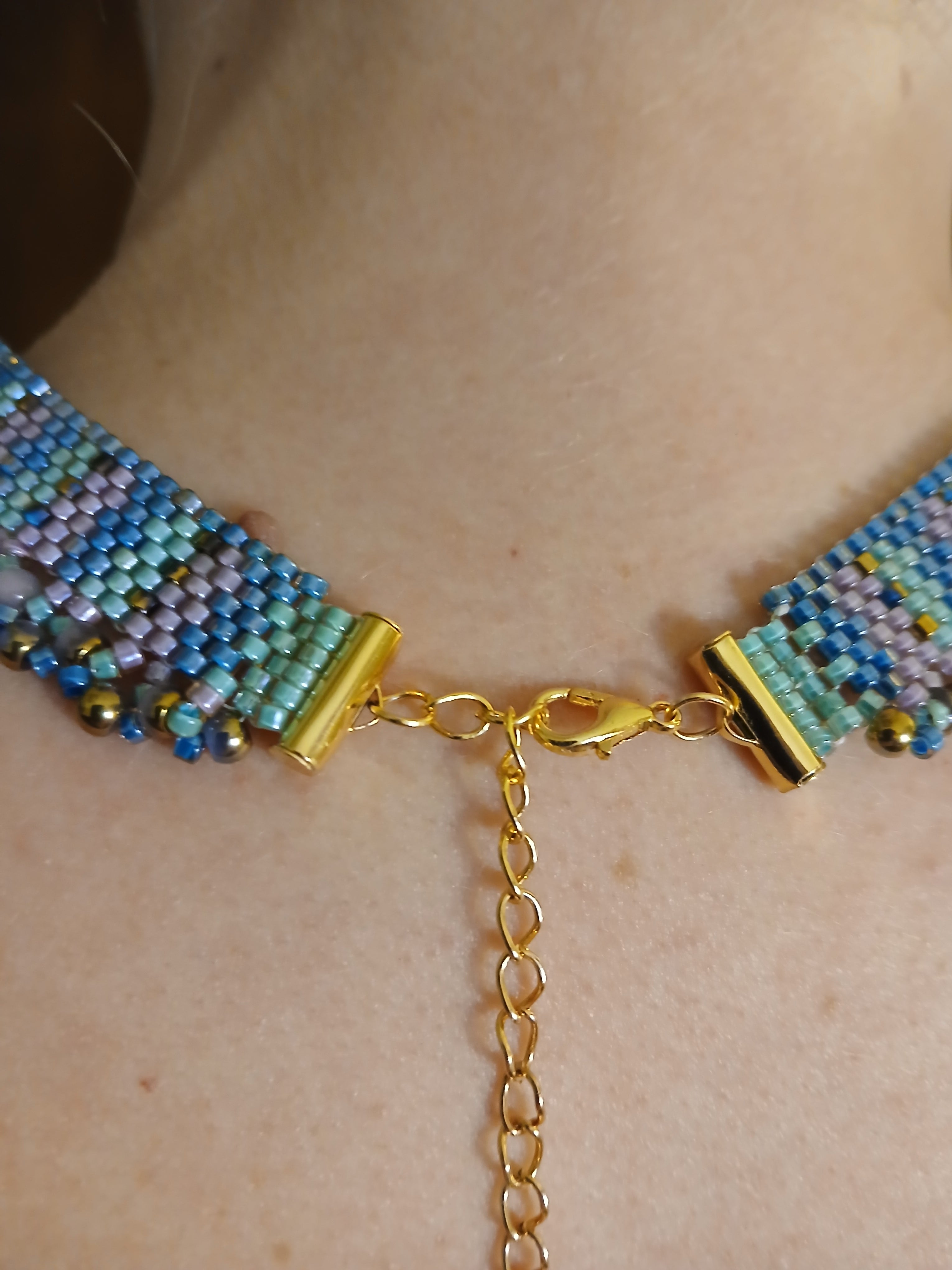 Handwoven choker in seafoam teal and purple from the Mermaid Finery Collection by Regina Creates, featuring a 3.5-inch bead pendant.

Closeup of lobster claw and extended chain closure on Model 